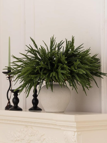 Artificial green Norfolk pine branch arrangement in a white planter on a shelf