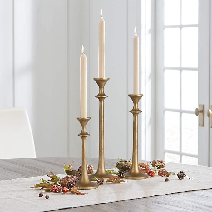 Brass iron taper candle holders holding three cream taper candles, tall and short.