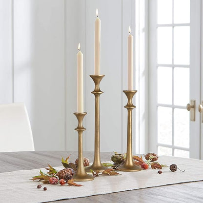 Brass iron taper candle holders holding three cream taper candles, tall and short.