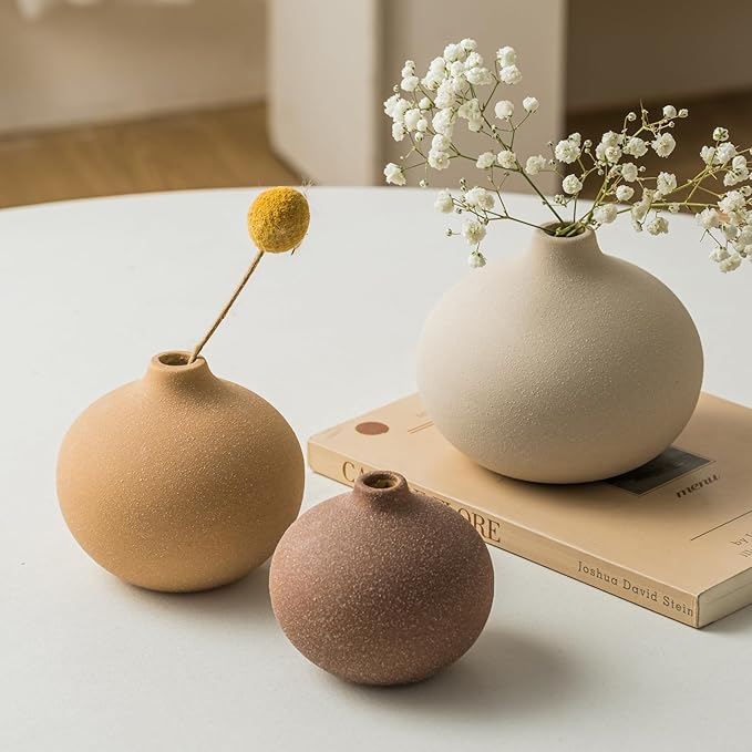 Matte ceramic bud vases with stems and blossoms arranged on stacked books