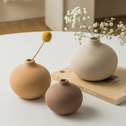 Matte ceramic bud vases with stems and blossoms arranged on stacked books