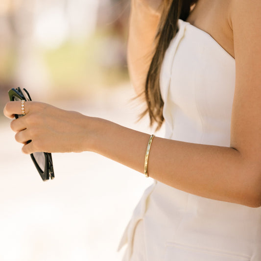 Gold-tone cuff bracelet on wrist, slim open bangle style