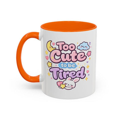 White mug with orange rim and handle, “Too Cute to be Tired” bunny graphic.