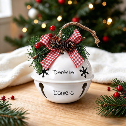 White holiday jingle bell ornament with red plaid bows, pine, and pinecone accents