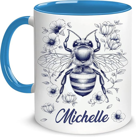 White ceramic bee mug with blue handle, floral bee graphic, and "Michelle" name