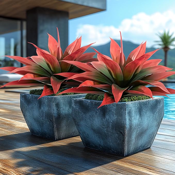Two red and green faux agave plants in blue fabric-like planters on a wooden deck
