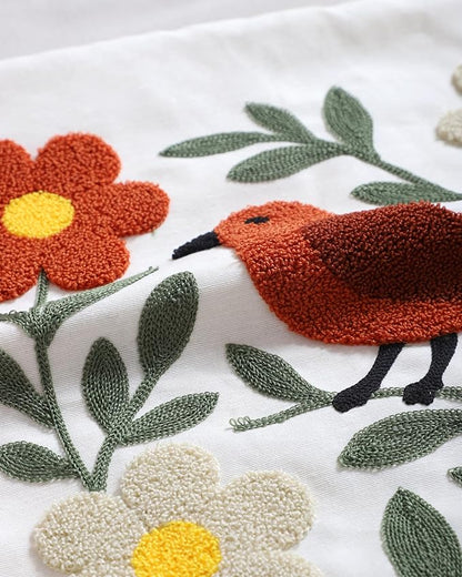 Punch-needle bird and flower embroidery detail on white pillow cover with green leaves