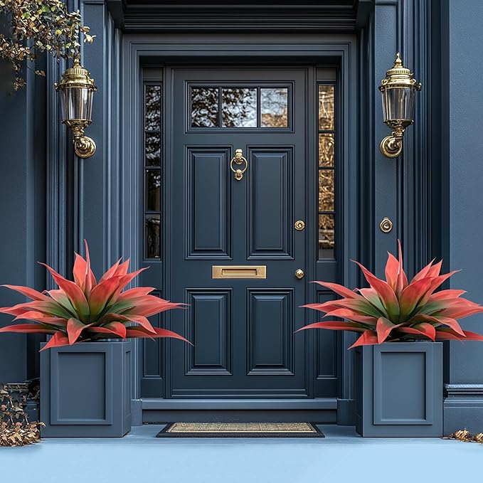 Two red and green faux agave plants in blue planters near a dark front door