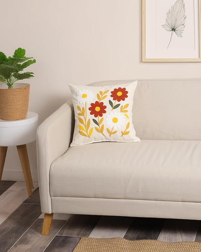 White pillow cover with embroidered daisies and red flowers on a sofa back