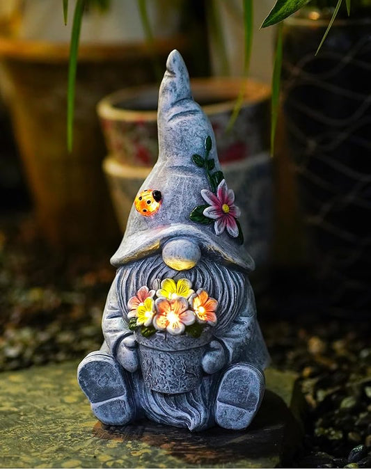 Goodeco sitting gnome statue in blue-gray holding flower, with glowing lantern light.