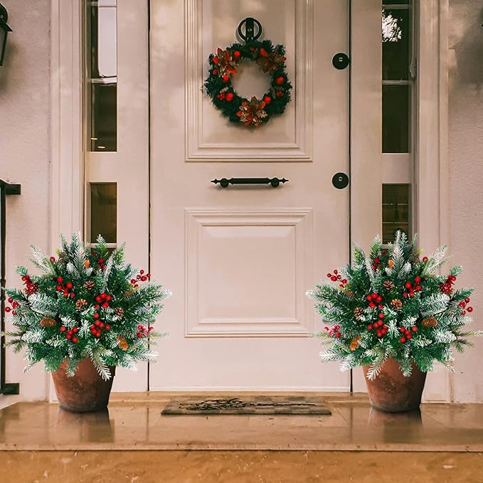 Two pre-lit artificial pine tree decorations with red berries and pine cones, planted in urns