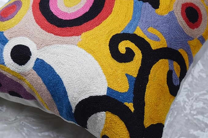 Close-up of multicolor embroidered pillow cover with abstract shapes in yellow, blue, purple, and black.