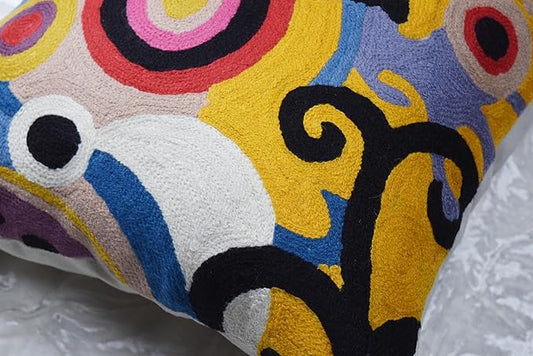 Close-up of multicolor embroidered pillow cover with abstract shapes in yellow, blue, purple, and black.