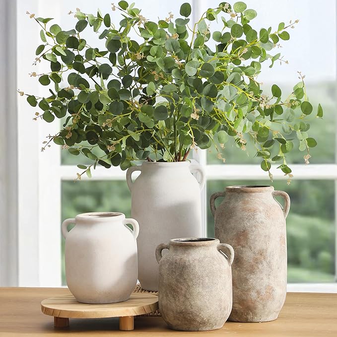 White ceramic vase with side handles holding leafy green stems on wooden stand