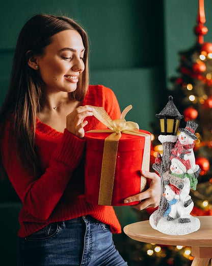 Lighted stacked snowman lantern figurine on table beside wrapped Christmas gift