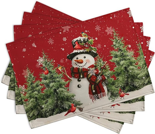 Four red Christmas placemats stacked, featuring a snowman, pine trees, and cardinals