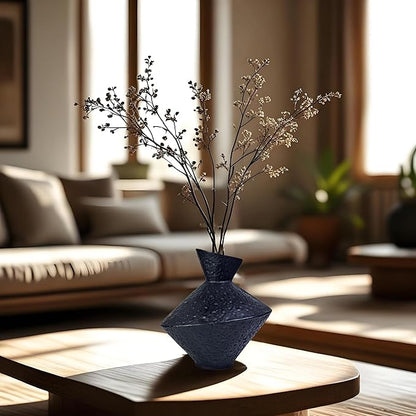Dark hammered cast iron vase on table with slender dried branches arrangement
