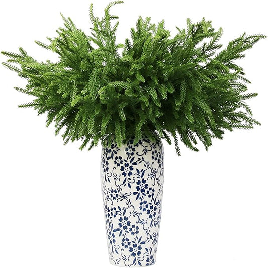 Artificial Norfolk pine branches with green needles in patterned white vase