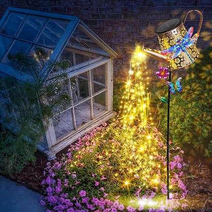 Solar watering can stake lights with dragonfly decorations, warm yellow glow by flower bed