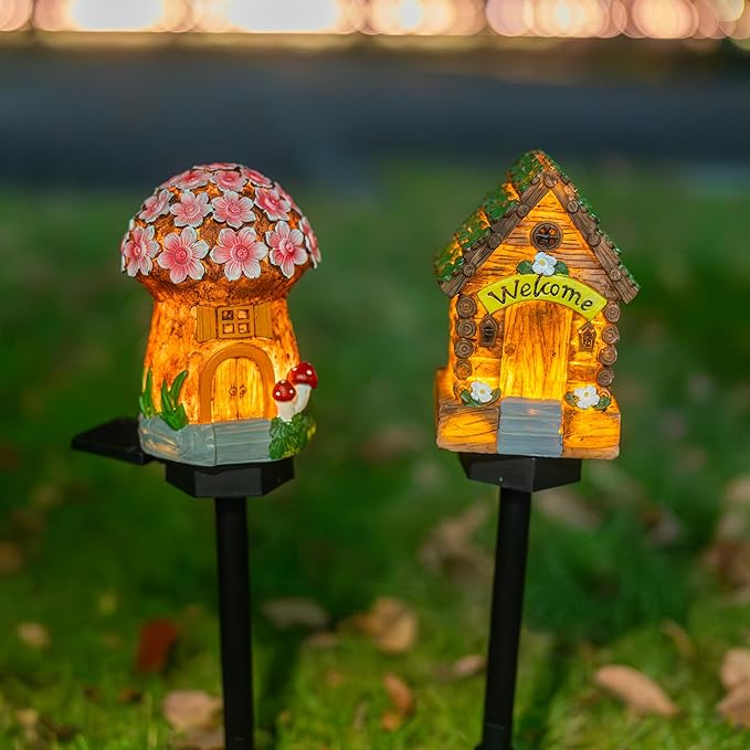 Two miniature garden lights on black stakes: a mushroom house and a glowing “Welcome” cottage.