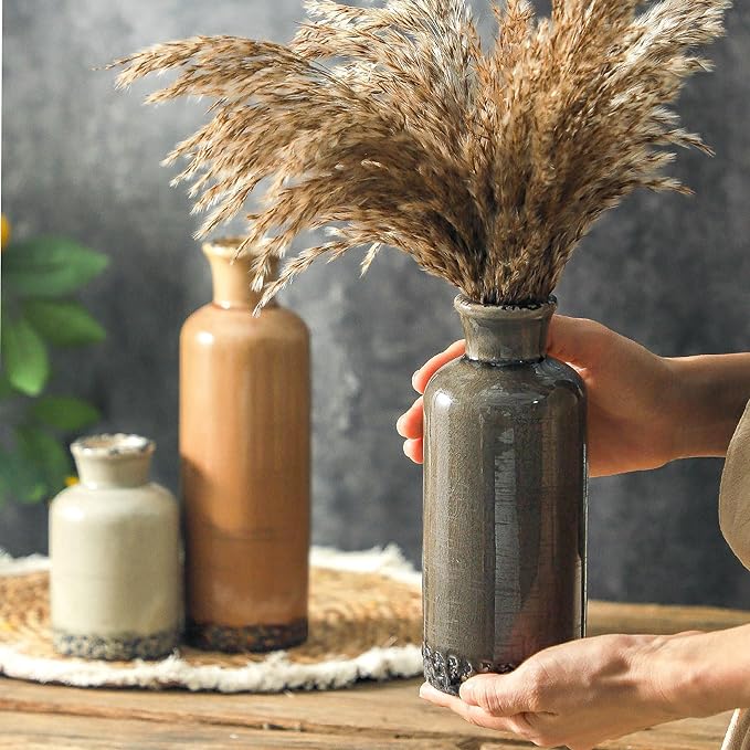 Three ceramic vases with dried stems: tall terracotta, gray, and cream on a tray