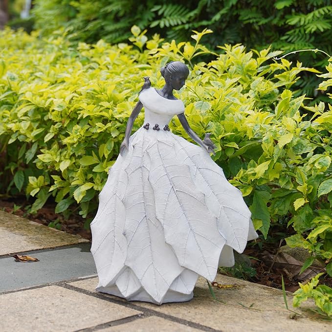 White resin fairy maiden statue beside green plants with layered skirt and bird figure