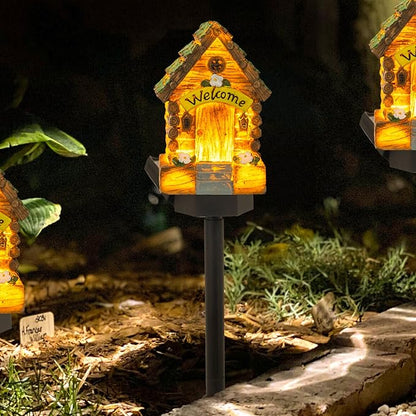 Glowing miniature fairy cottage house garden light on a black stake, “Welcome” on front.