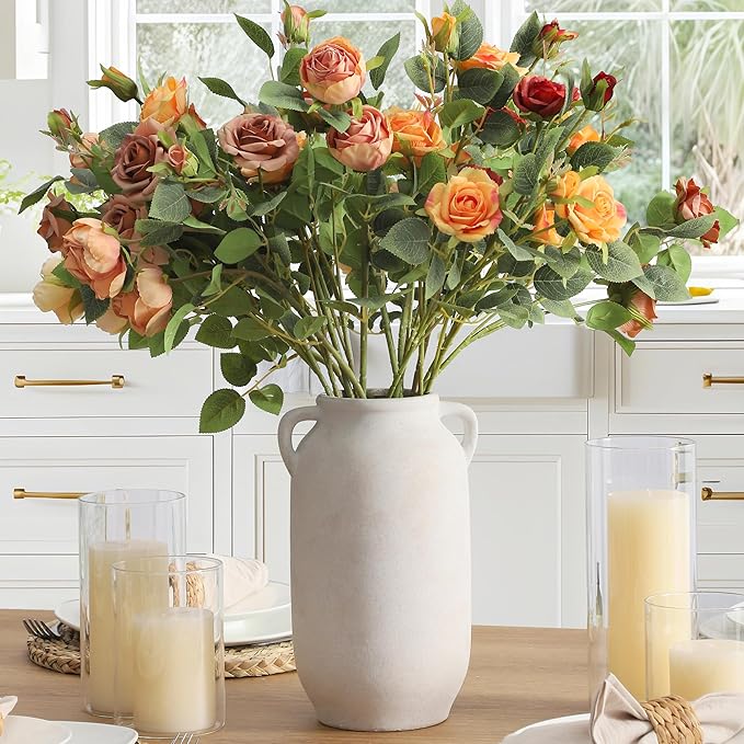 White ceramic vase with side handles holding orange and pink roses with greenery