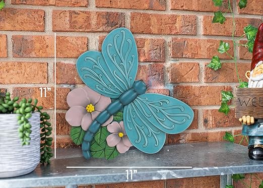 Teal blue dragonfly stepping stone with raised wings and pink flowers on patio surface