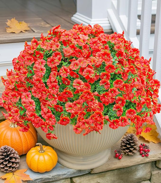 Faux orange daisy-style flower pieces with green leaf accents in a round planter
