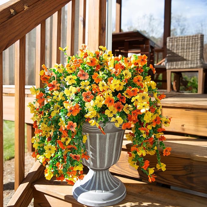 Artificial flower arrangement with orange and yellow blossoms and dangling green leaf strands