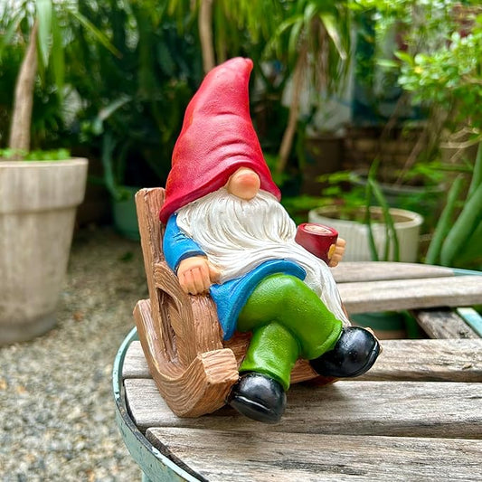 Garden gnome statue holding a mug while seated on wooden rocker, white beard, red hat
