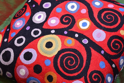 Red and black pillow cover with dense multicolor spiral, ring, and dot pattern.