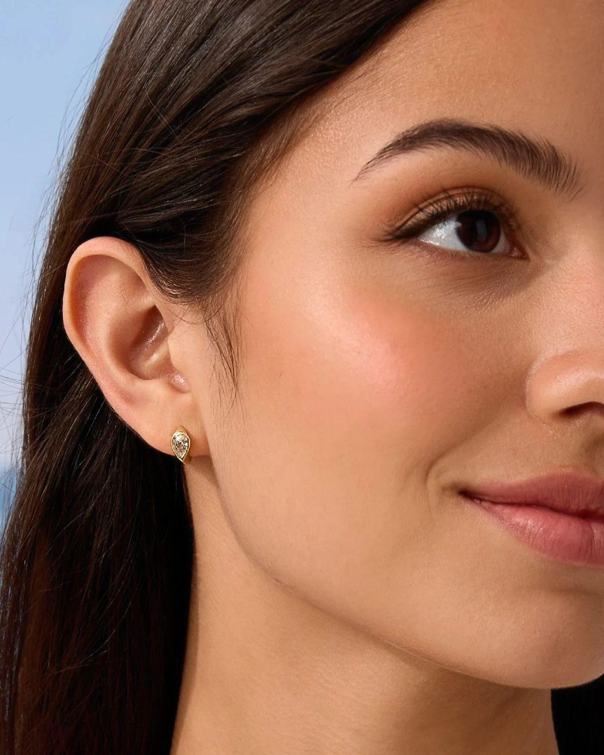 Small gold-tone hoop earring with clear stone, side face close-up