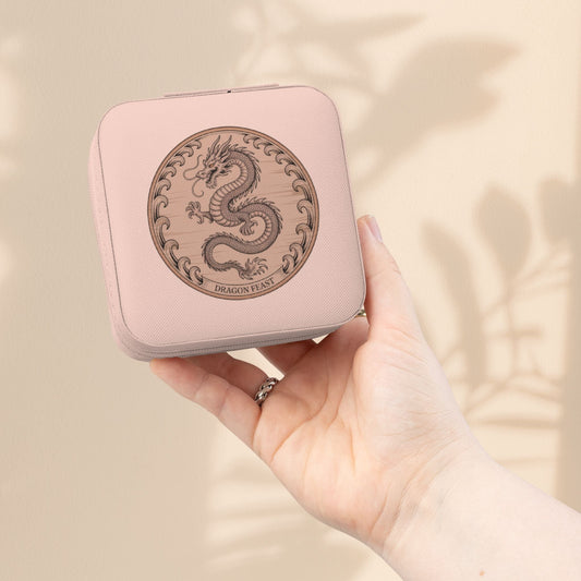 Compact jewelry travel case in light pink with dragon emblem, held in hand.