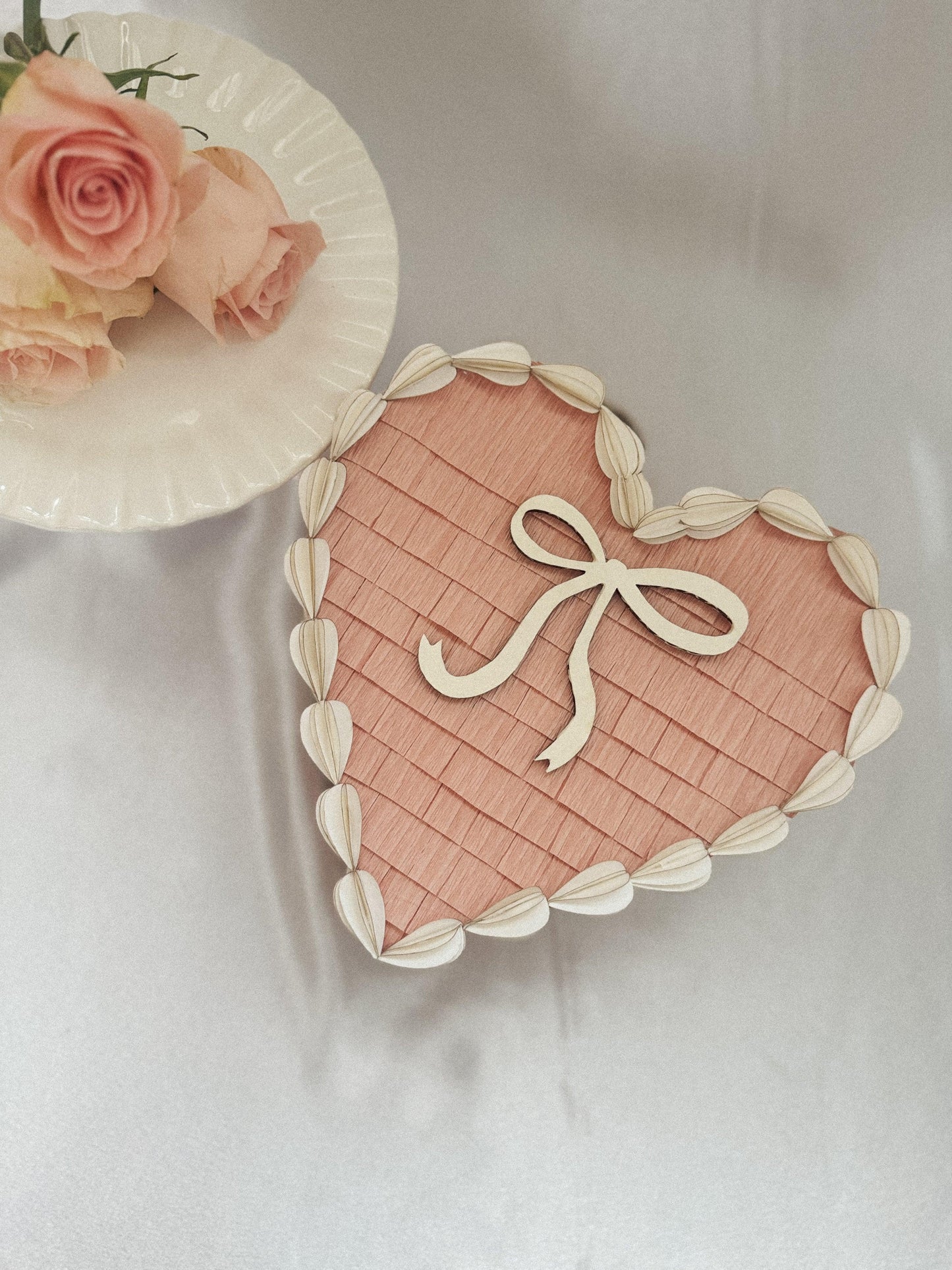 Piñata de corazón San Valentín rosa con lazo blanco y borde de hojas en crema