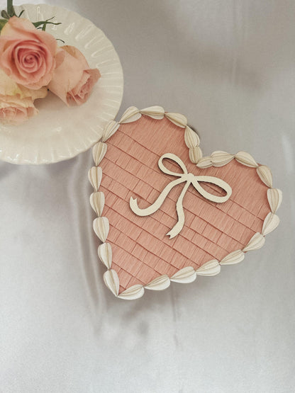 Piñata de corazón San Valentín rosa con lazo blanco y borde de hojas en crema