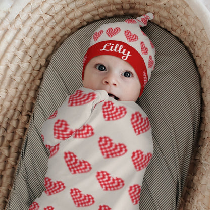 Baby swaddled with red heart-print blanket and matching hat