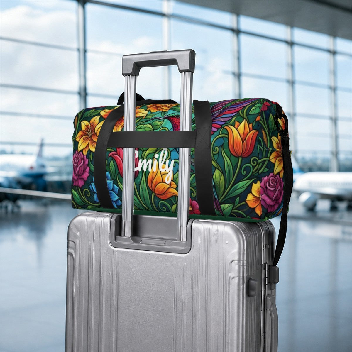 Floral duffel bag with black straps and Emily logo, on a rolling suitcase handle