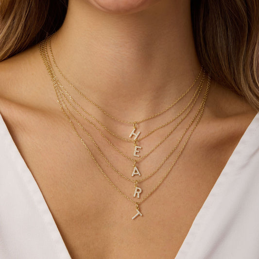 Gold diamond letter necklaces with H, E, A, R, and X pendants on layered chains