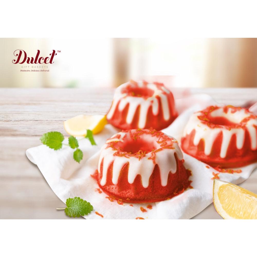 Red-glazed bundt cakes on parchment with garnish and a lemon slice