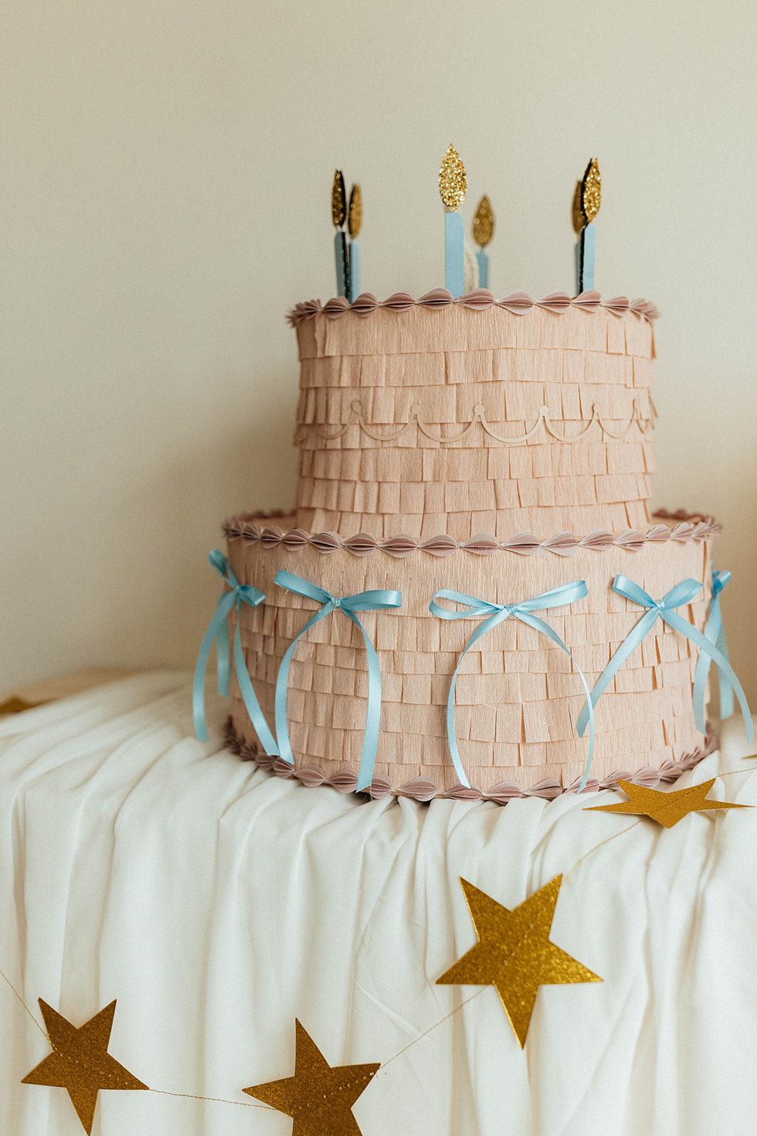 Piñata pastel rosa con velas doradas y lazos azules, diseño de dos pisos