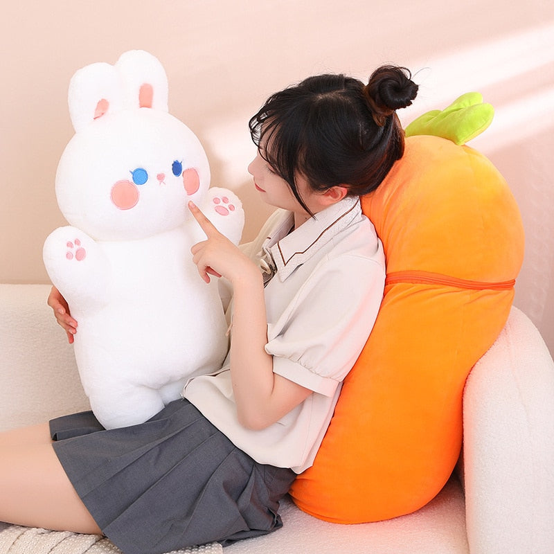 Two fruit animal plush toys: white bunny and orange carrot pig on a couch