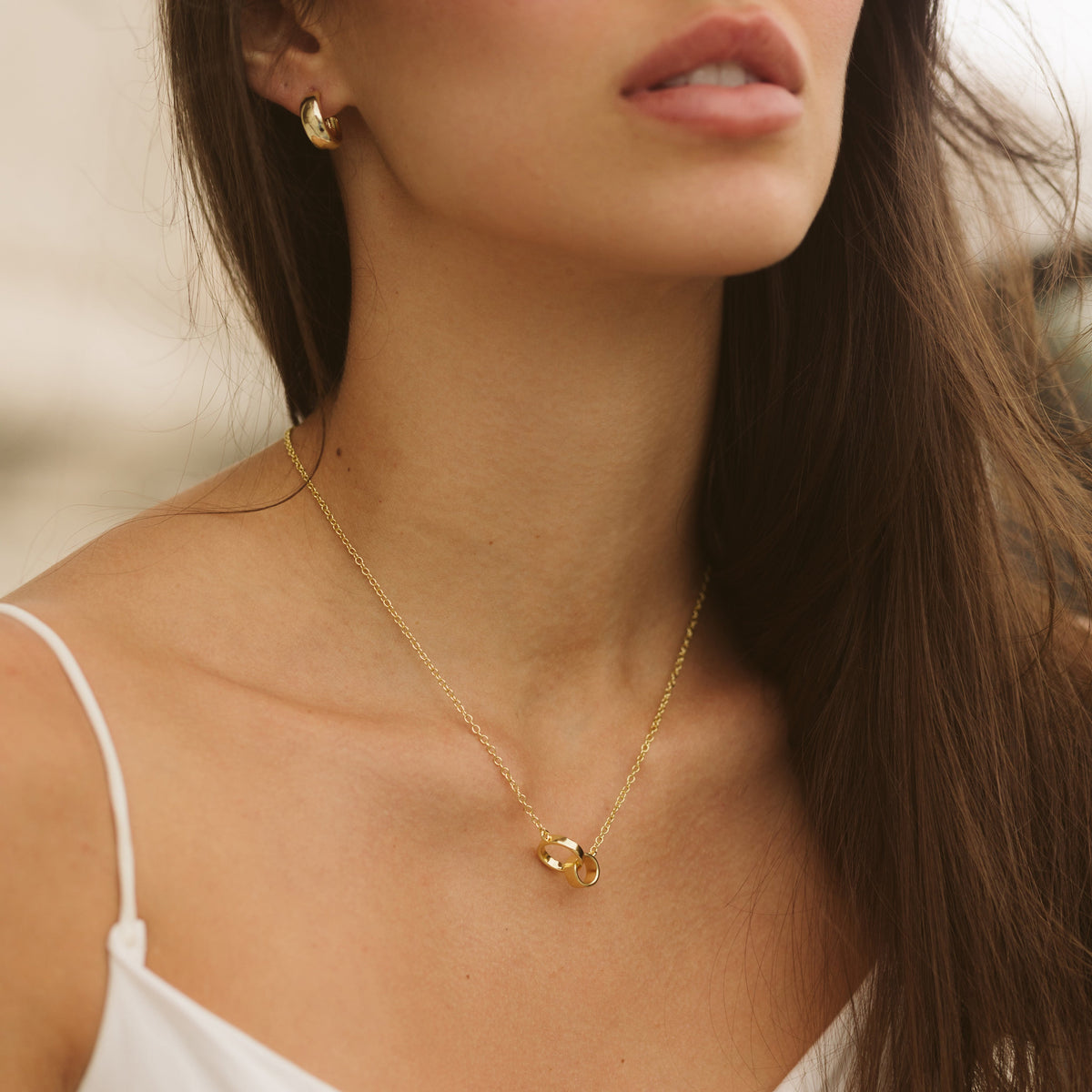Gold-tone interlocking ring charm necklace resting on collarbone