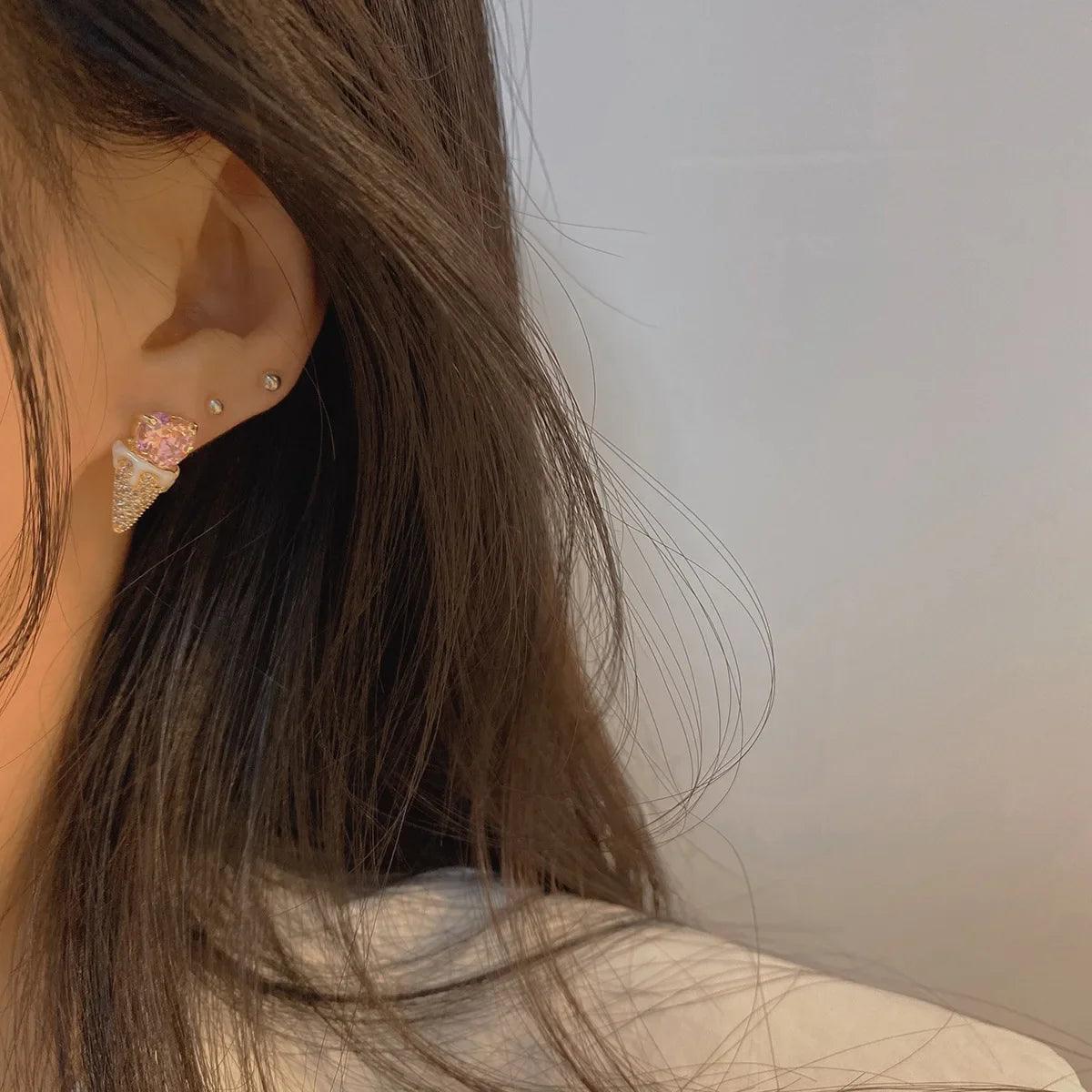 Pink heart top earrings with gold-tone triangular glitter, worn on ear