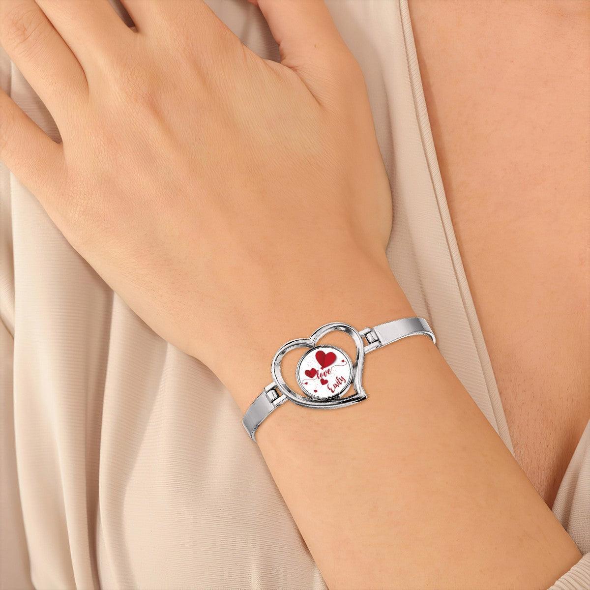 Heart charm bracelet on wrist with silver band and locket reading "Love Emily"