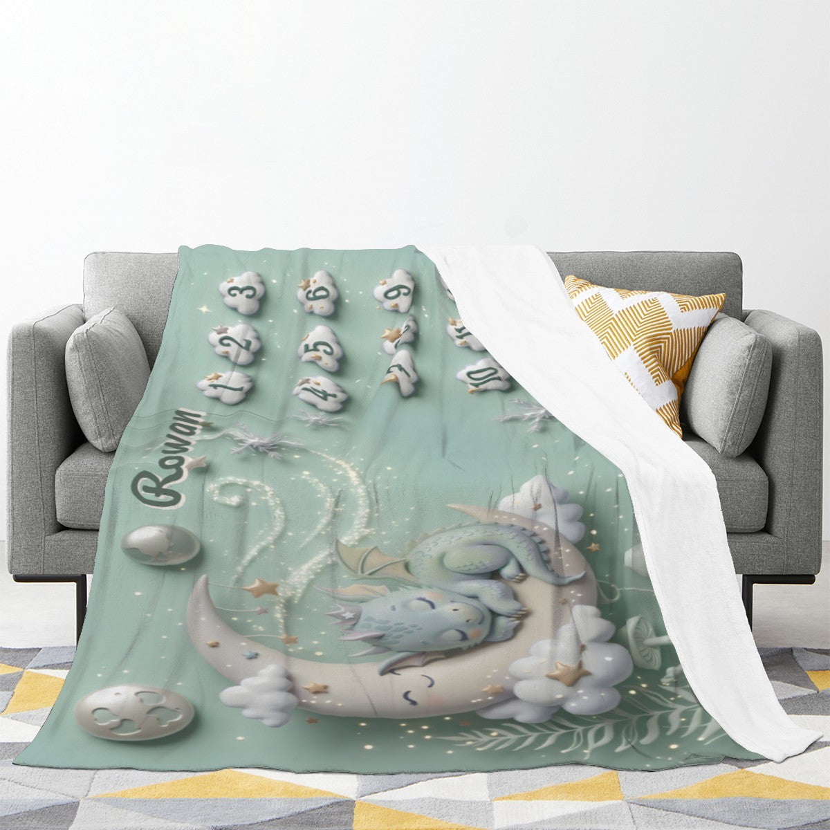 Mint baby milestone blanket draped over sofa with sleeping dragon and numbered “Months” design