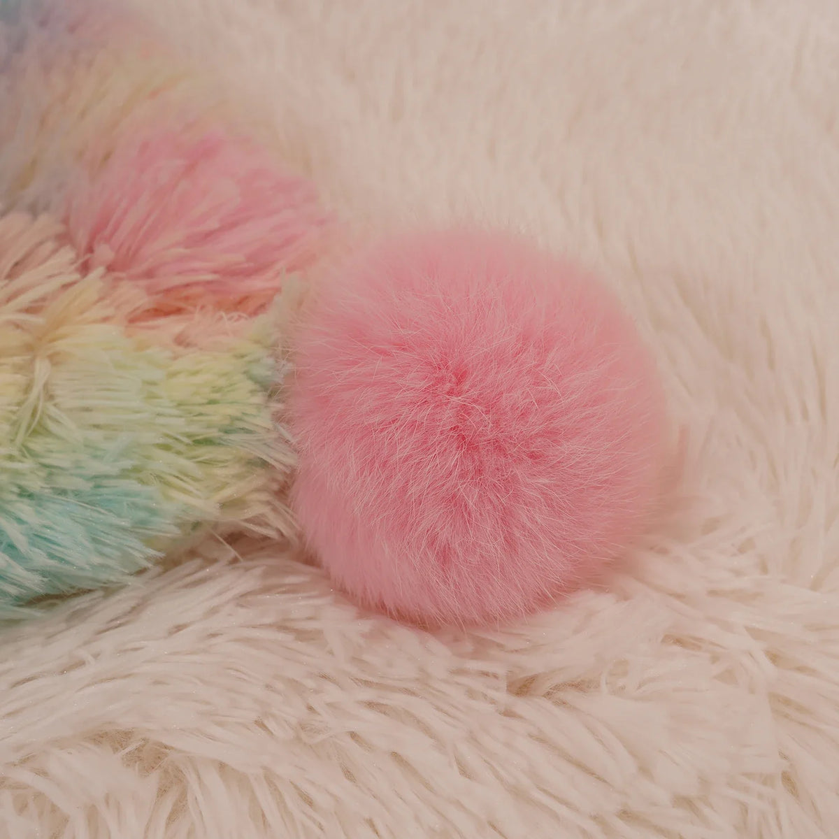 Soft pastel pom-pom on the corner of a fluffy rainbow blanket
