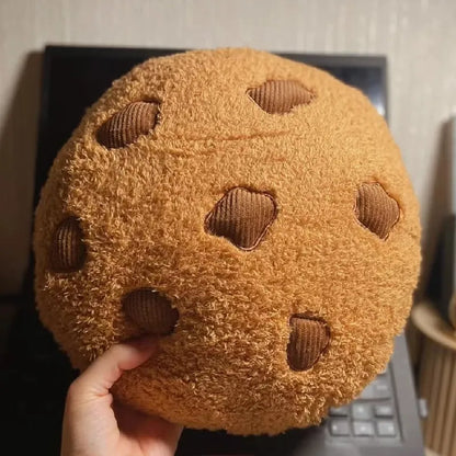 Round tan cookie plush pillow with brown stitched chocolate-chip shapes, held up