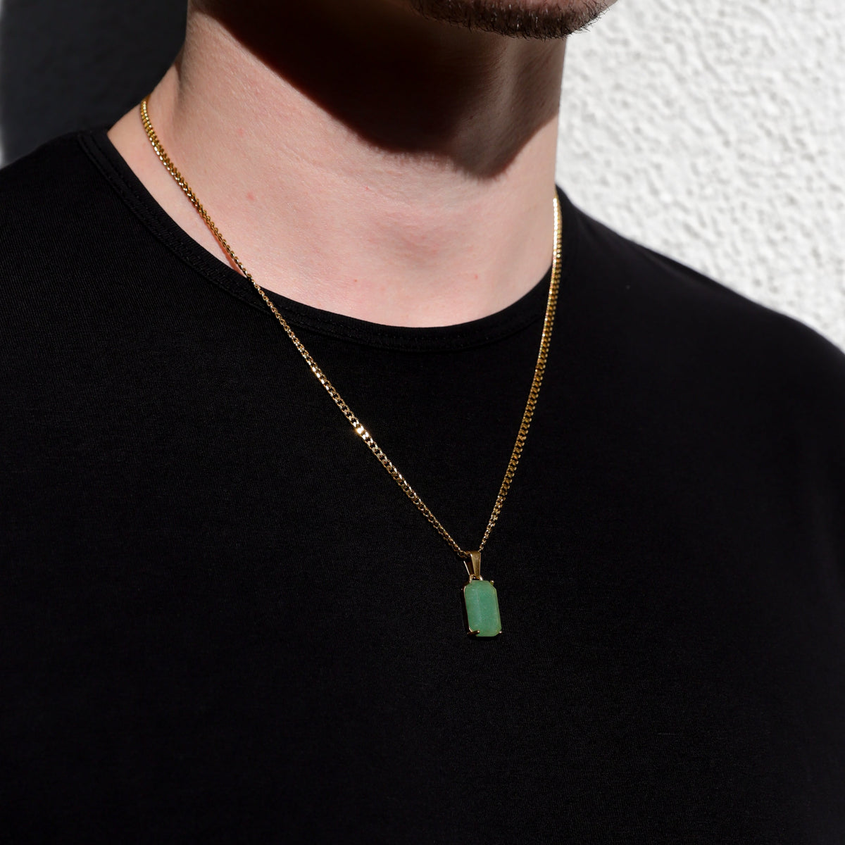 Gold chain necklace with green rectangular stone pendant, close-up on neckline